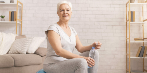 cheerful-senior-woman-drinking-water-on-fitball-free-space